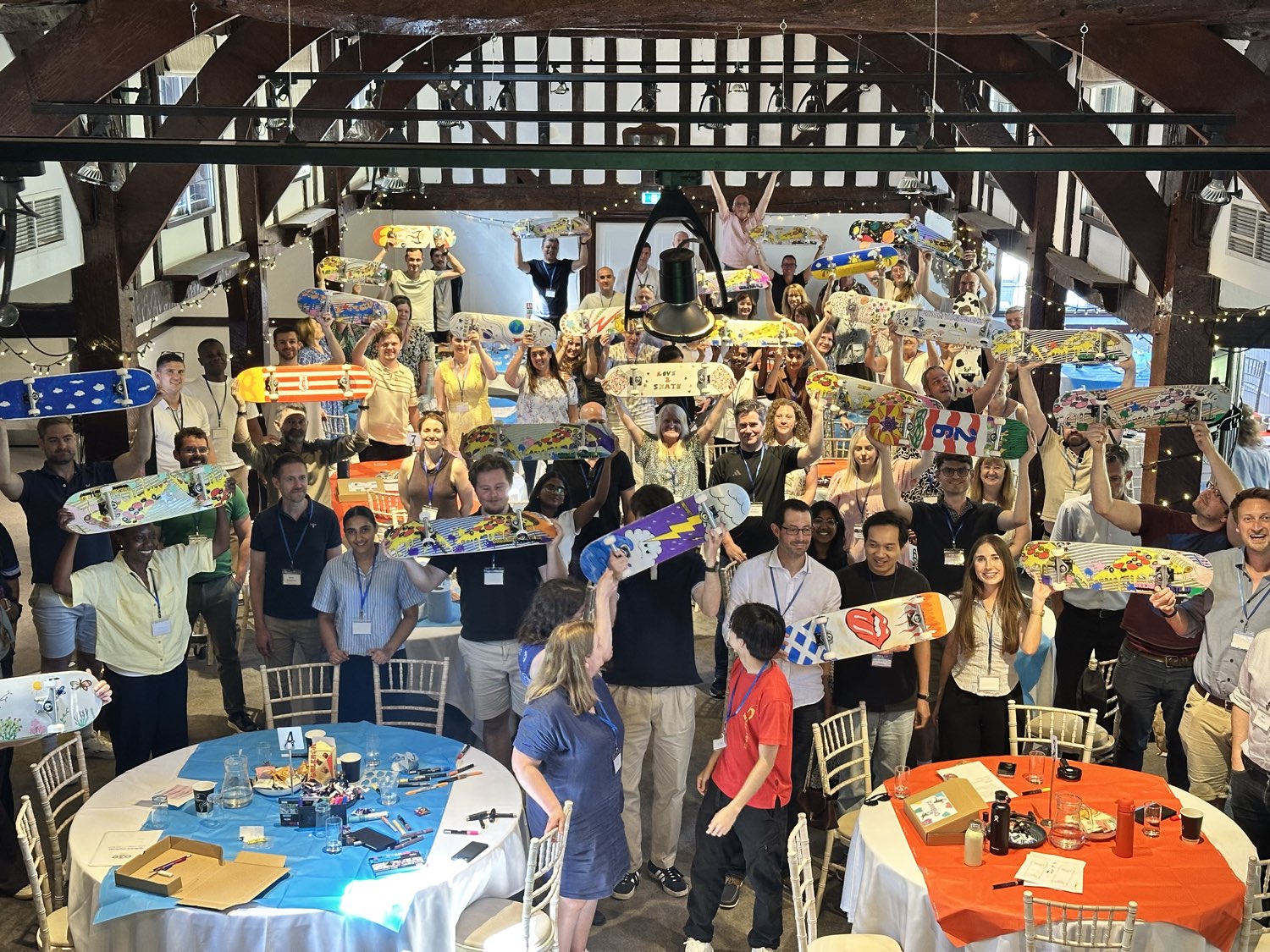 A large hall of people at tables with the skateboards they have decorated